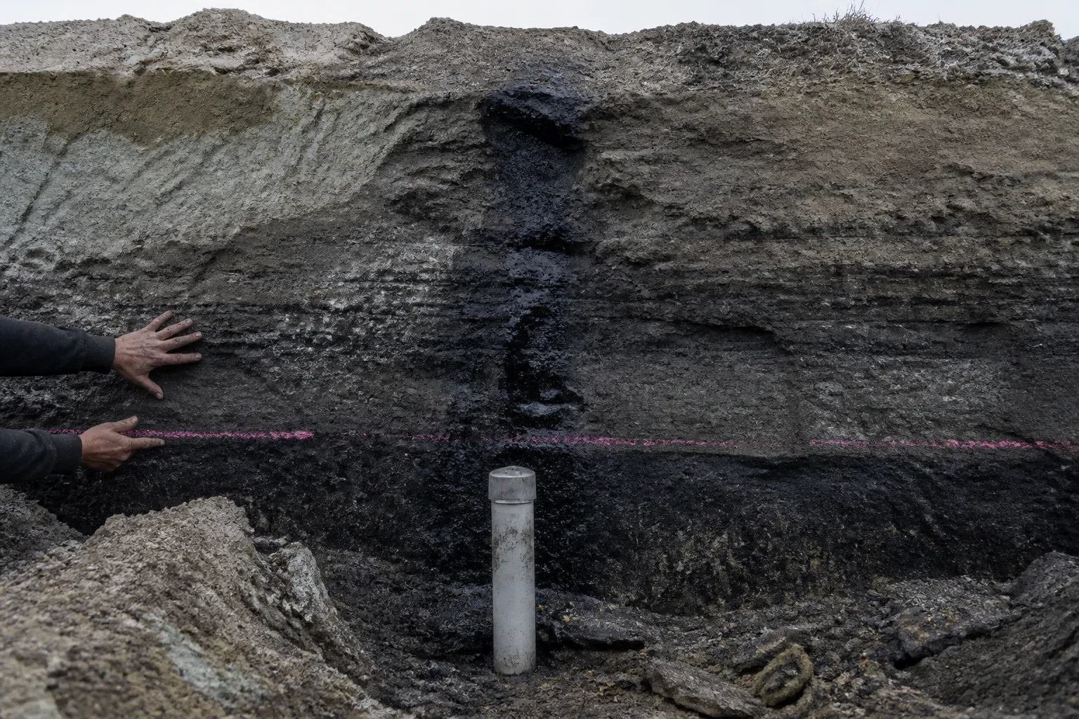 Fresh trench wall with capped monitoring well and survey-pink interval line