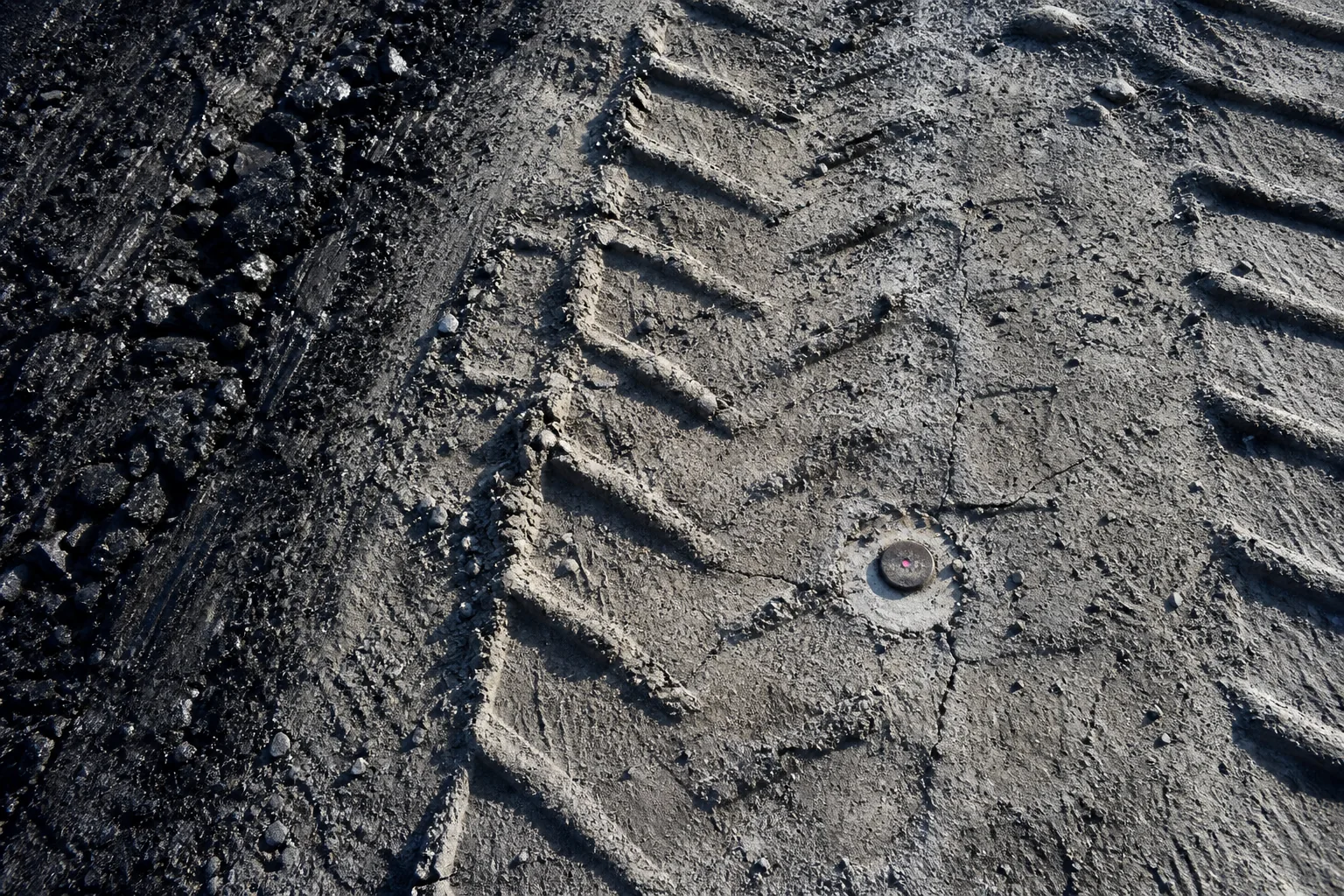 Stripped mine bench floor with tyre impressions ending at a survey plug