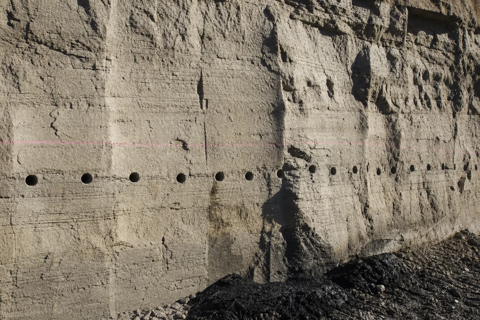 Pink-datum-marked drilled sandstone face with wet black cuttings