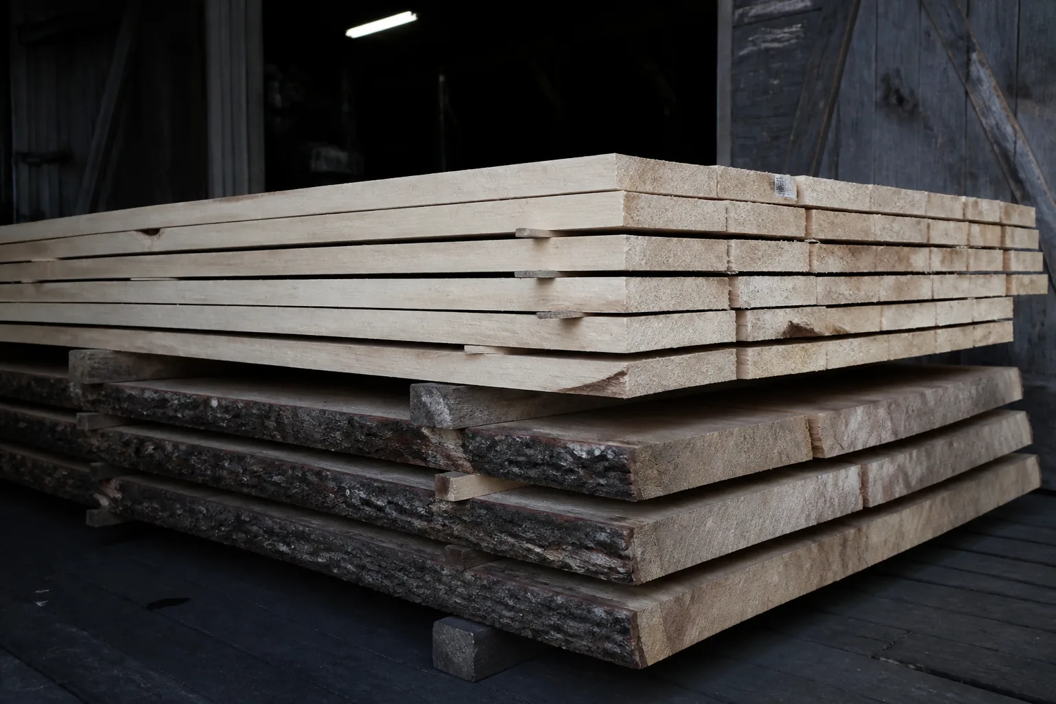 Fresh sawn boards stacked over bark-edged cants inside a sawmill load-out
