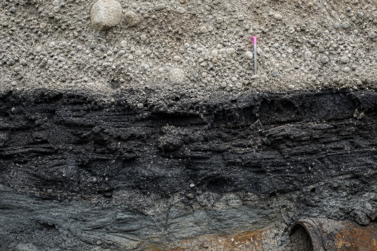 Road-cut exposure of gravel embankment over compressed peat